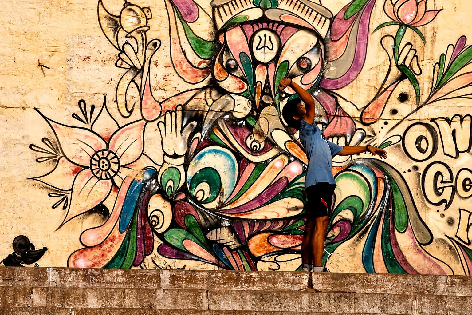 A badminton player reaches overhead in front of a painted Ganesha mural in Varanasi, photographed in 2014