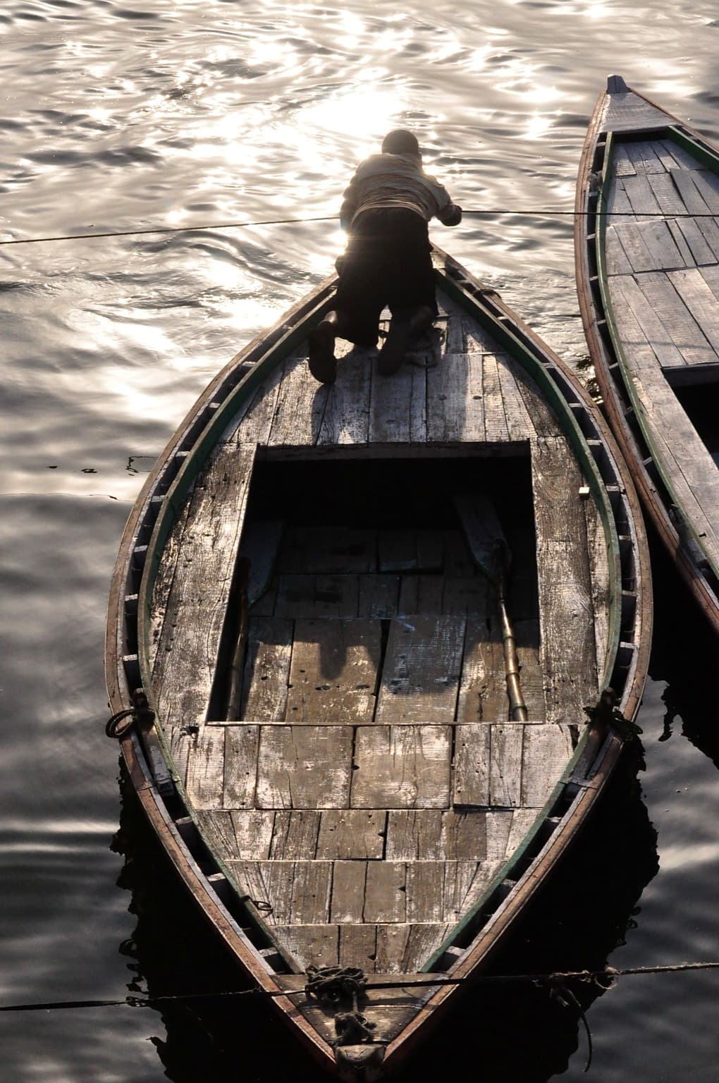 A man kneels in a wooden rowboat on luminous morning water on the Ganges at Varanasi, photographed in 2014