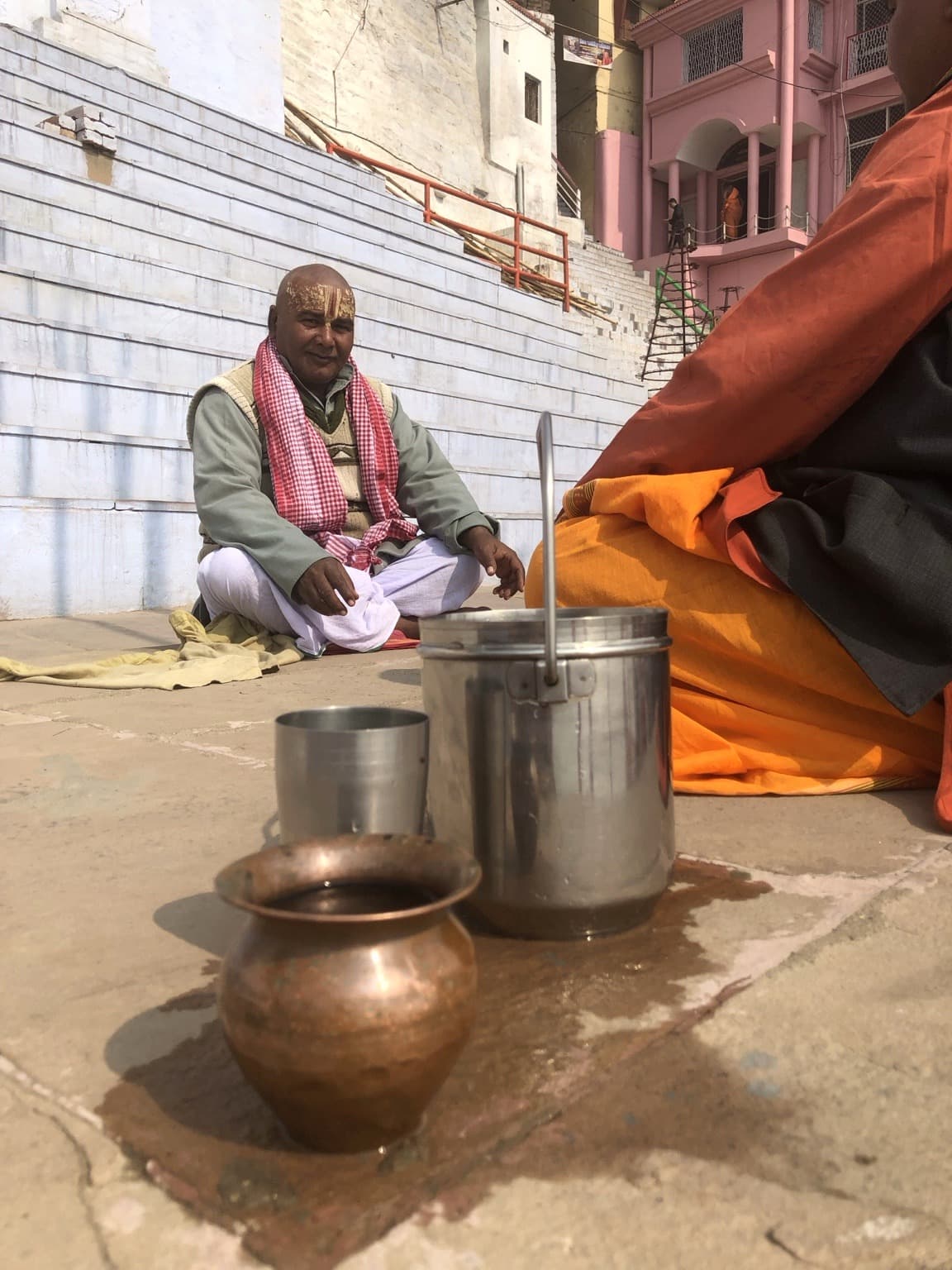 Metal vessels occupy the foreground while men sit on the ghats behind them, Varanasi, 2019