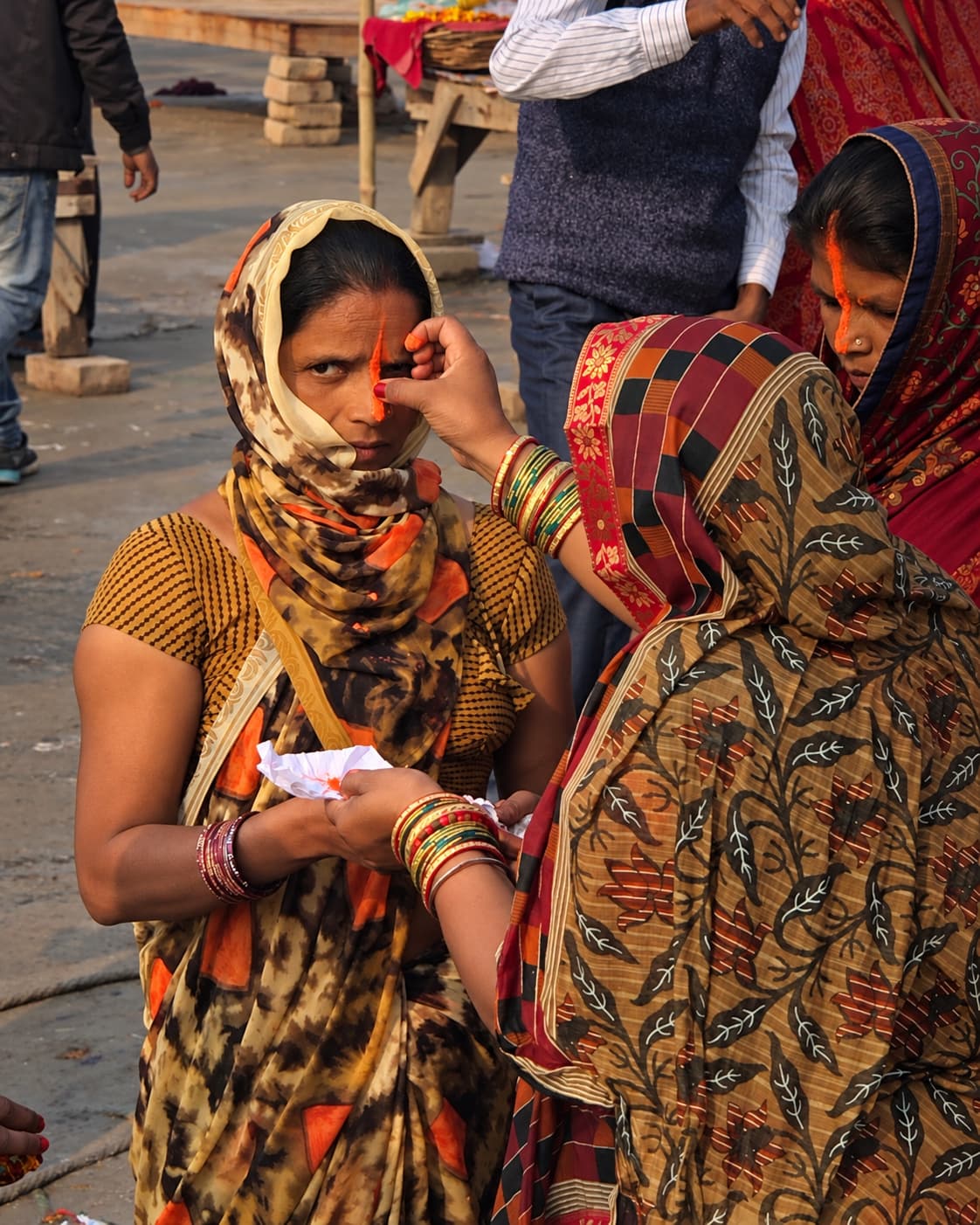 A woman applies orange pigment to another woman’s forehead as the recipient looks toward the camera in Varanasi, 2019