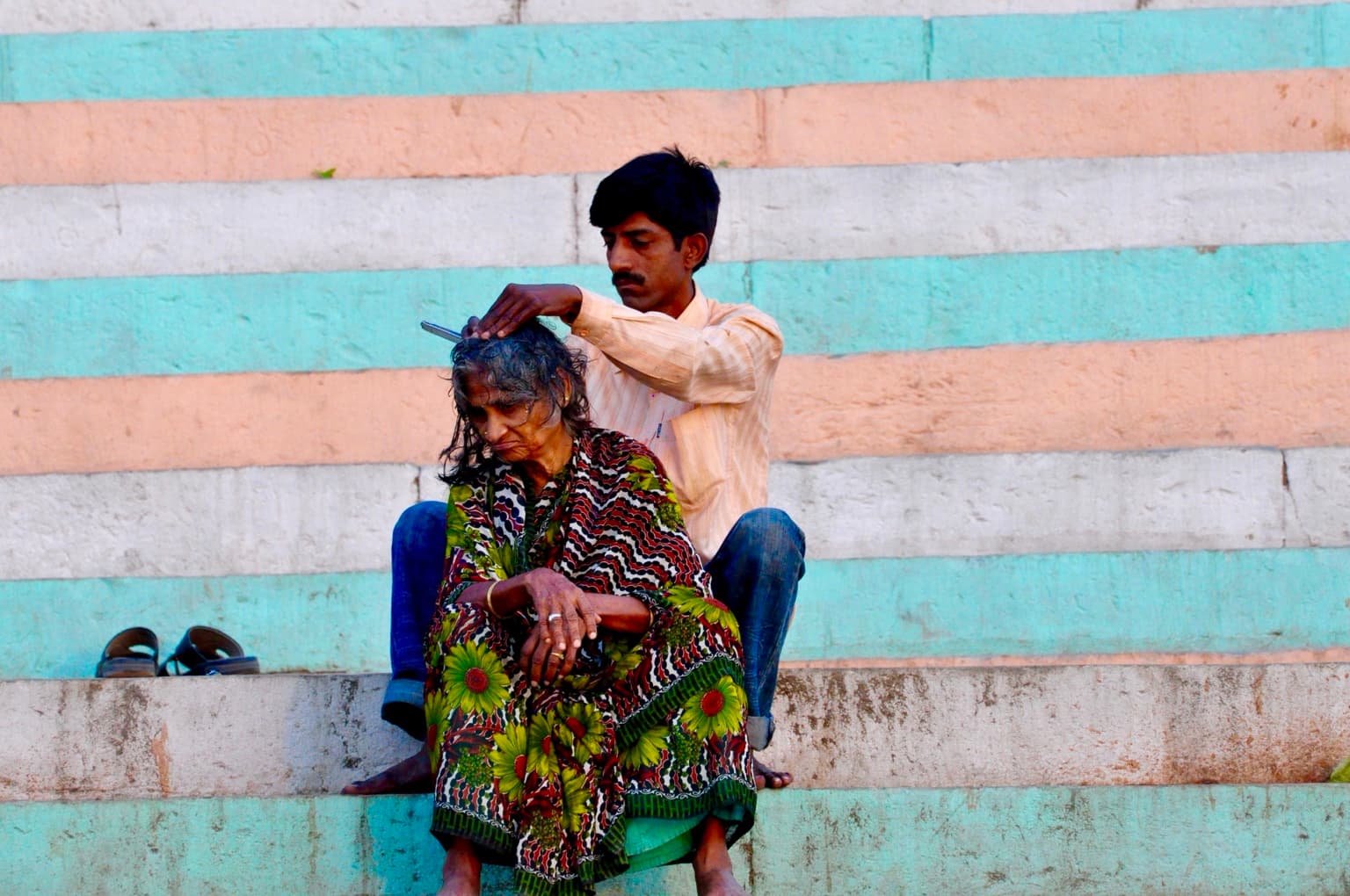 A man tends a seated woman’s hair on painted steps of the ghats in Varanasi, photographed in 2014
