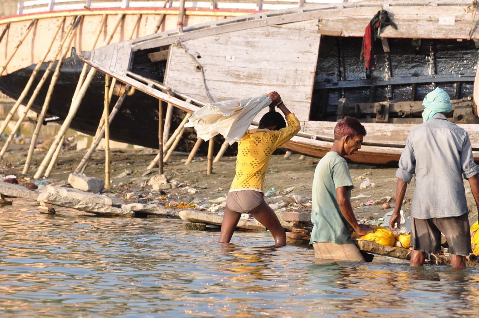 Workers washing cloth beside large wooden boats on the riverfront in Varanasi.