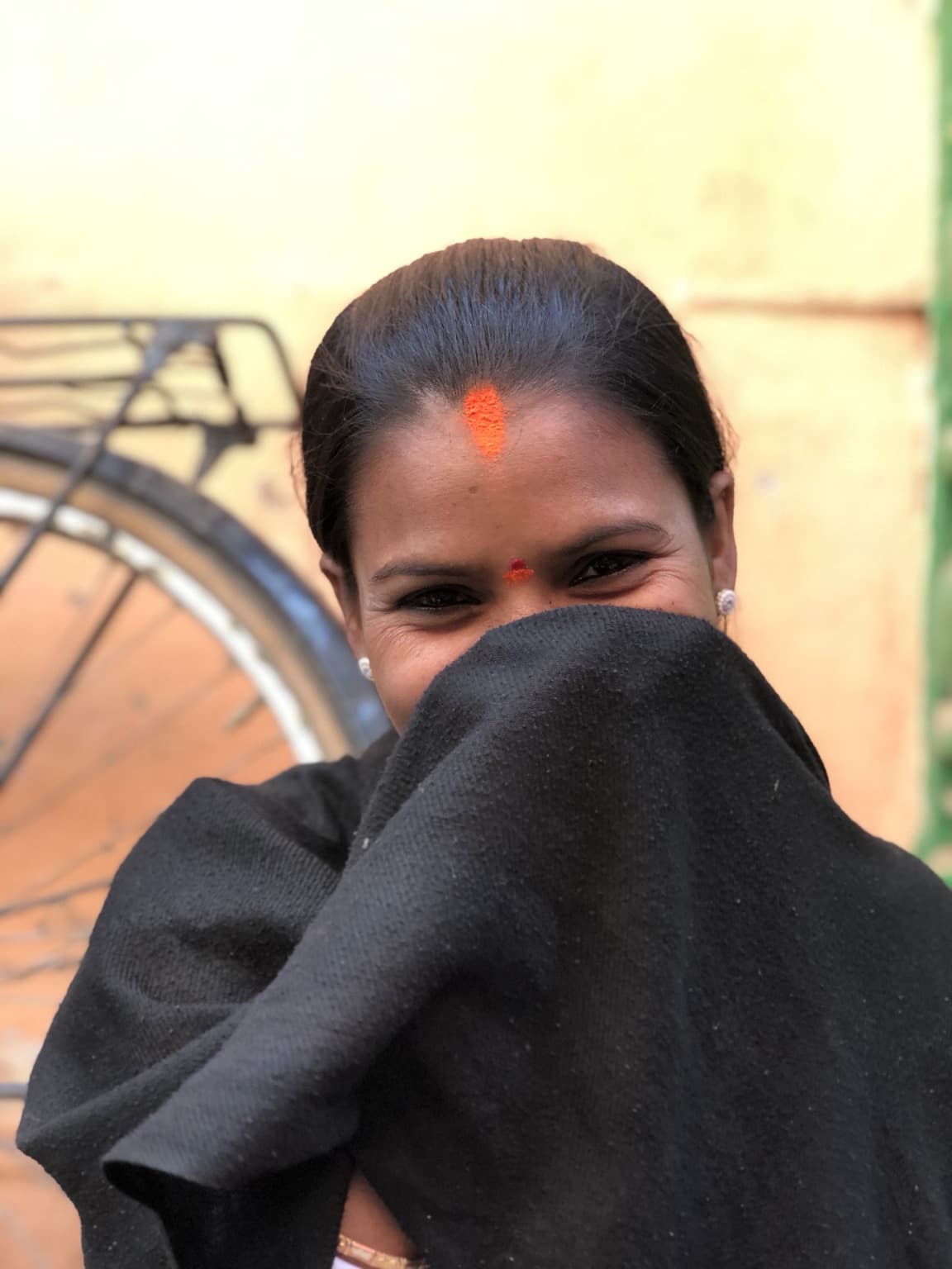 Woman looking toward the camera while holding a black shawl across the lower half of her face.