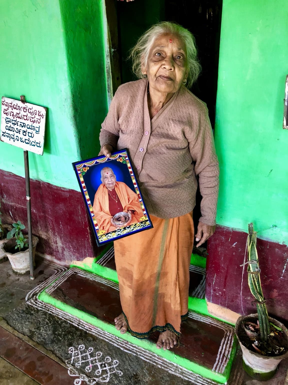 Woman standing in a green doorway holding a framed portrait of her deceased husband.