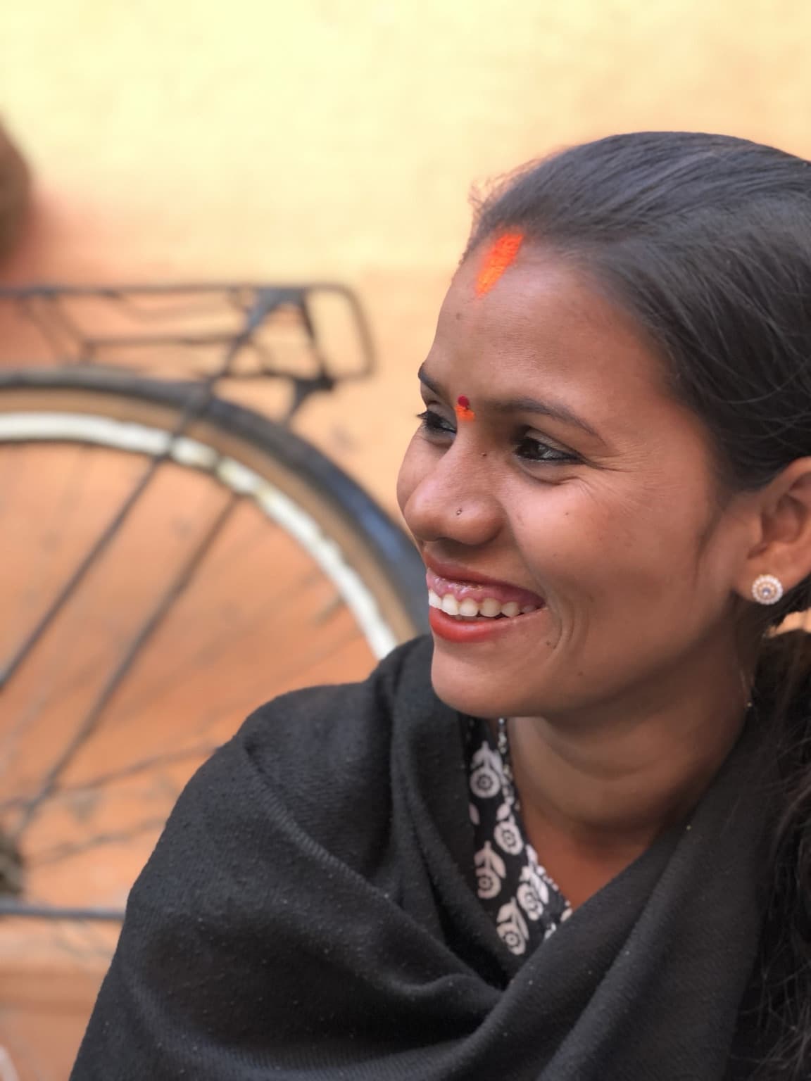 Woman smiling with her face uncovered, turned slightly to one side, with a bicycle behind her.