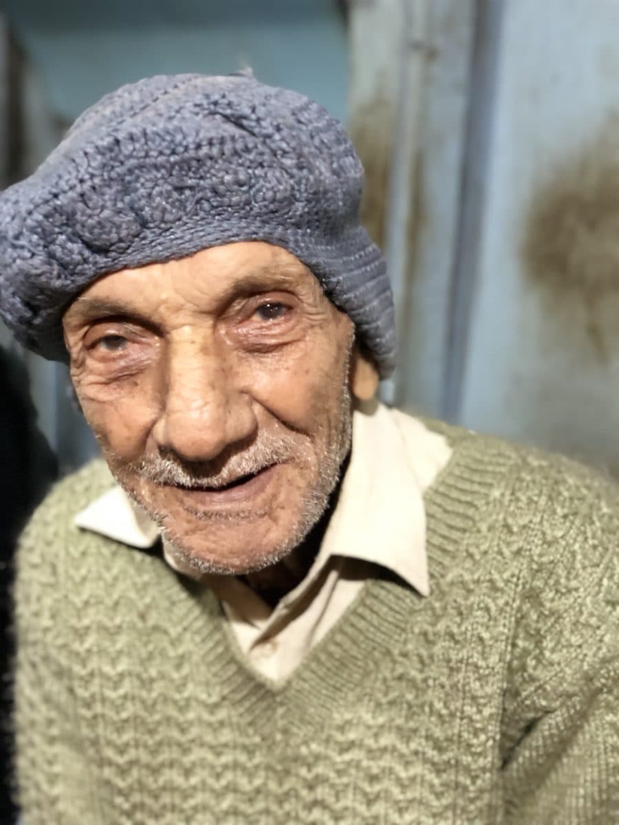 Close portrait of an older man in a knitted cap and green sweater at the tea stall.