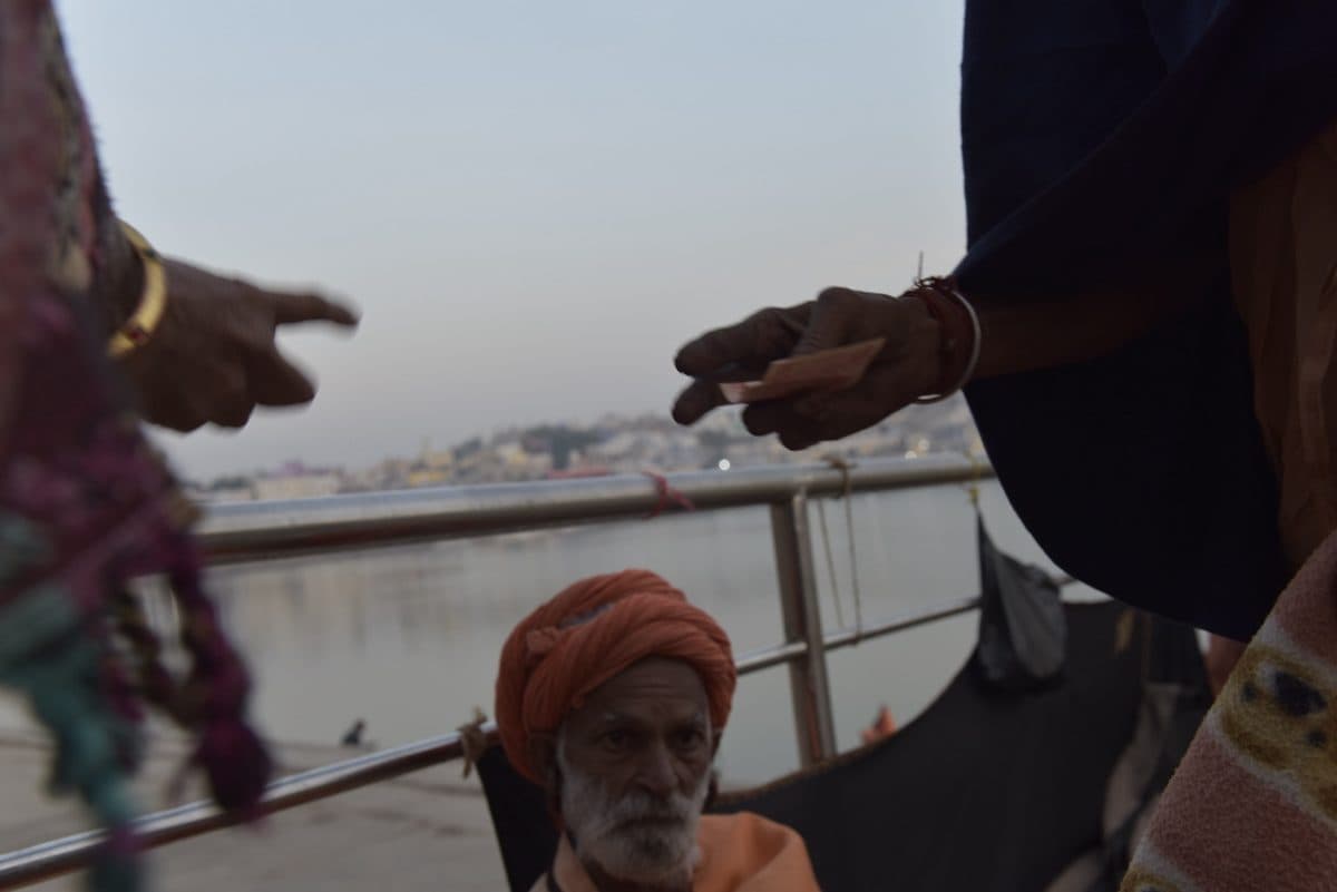 Gesturing hands beside the lake, with a seated man in an orange turban below.