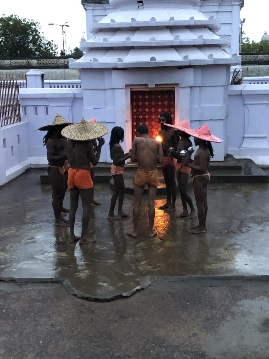 Group gathered in front of an illuminated shrine on wet pavement.