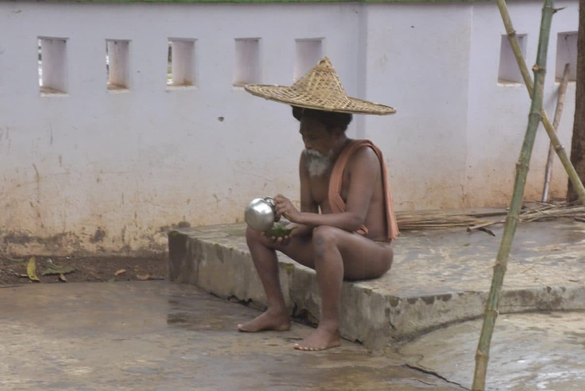 Seated man holding a vessel beside a courtyard wall.