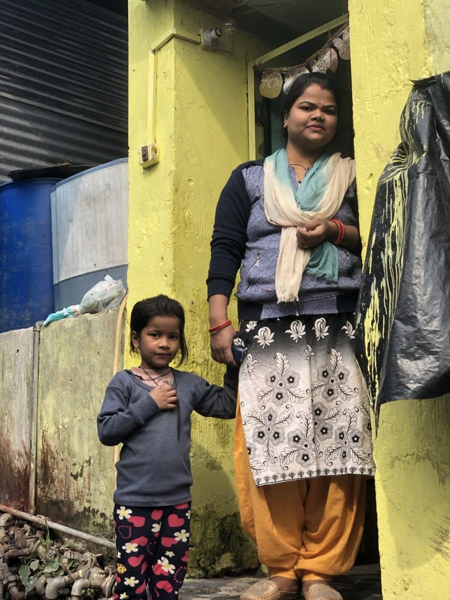 A woman and young girl standing outside a yellow doorway.