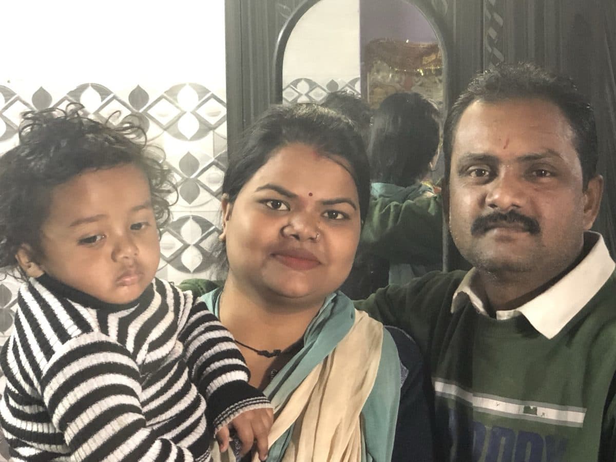 Woman and man with a young child in front of a mirror; the photographer is faintly reflected behind them.